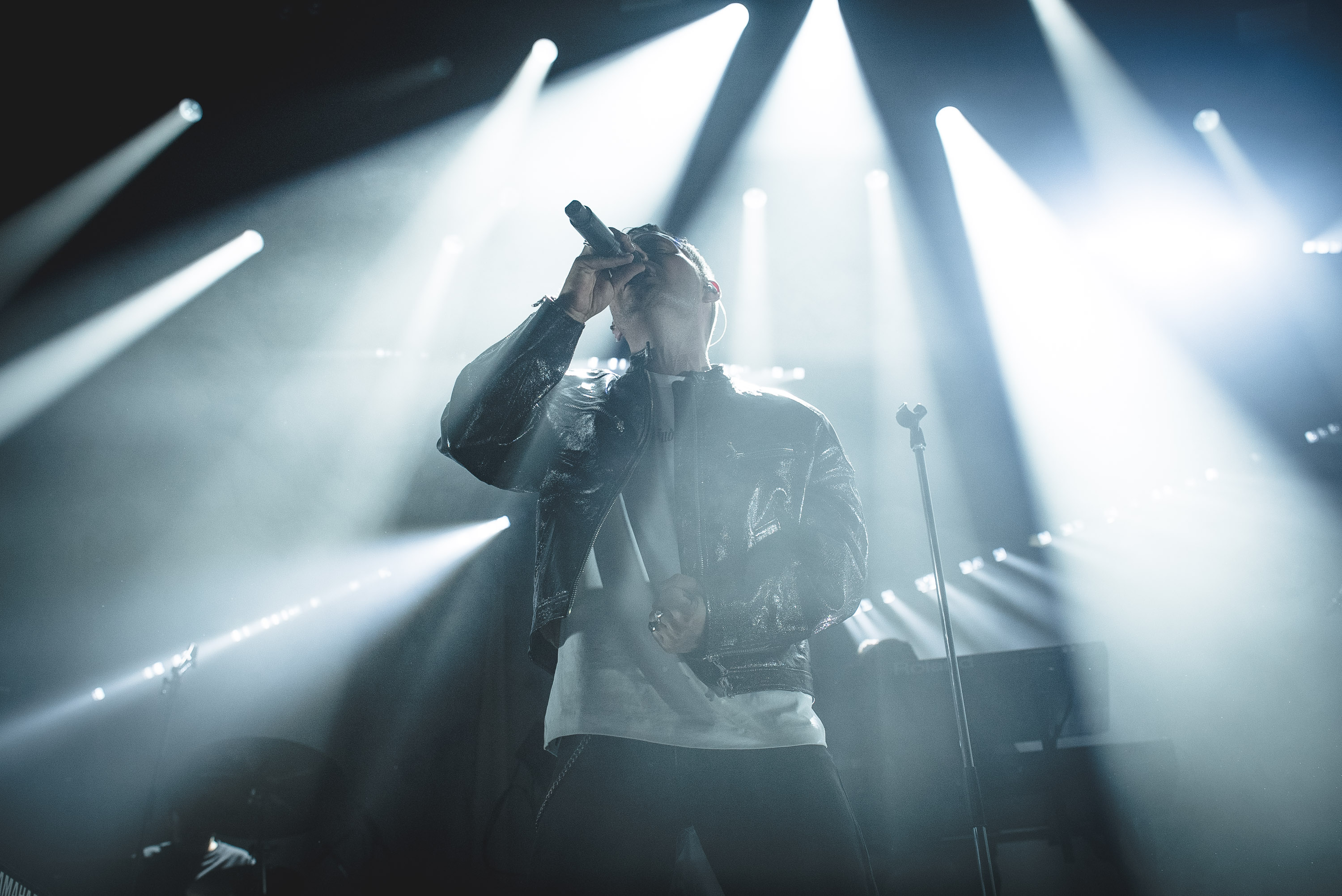 Oskar Linnros singing beneath white stage lights at Gasklockorna
