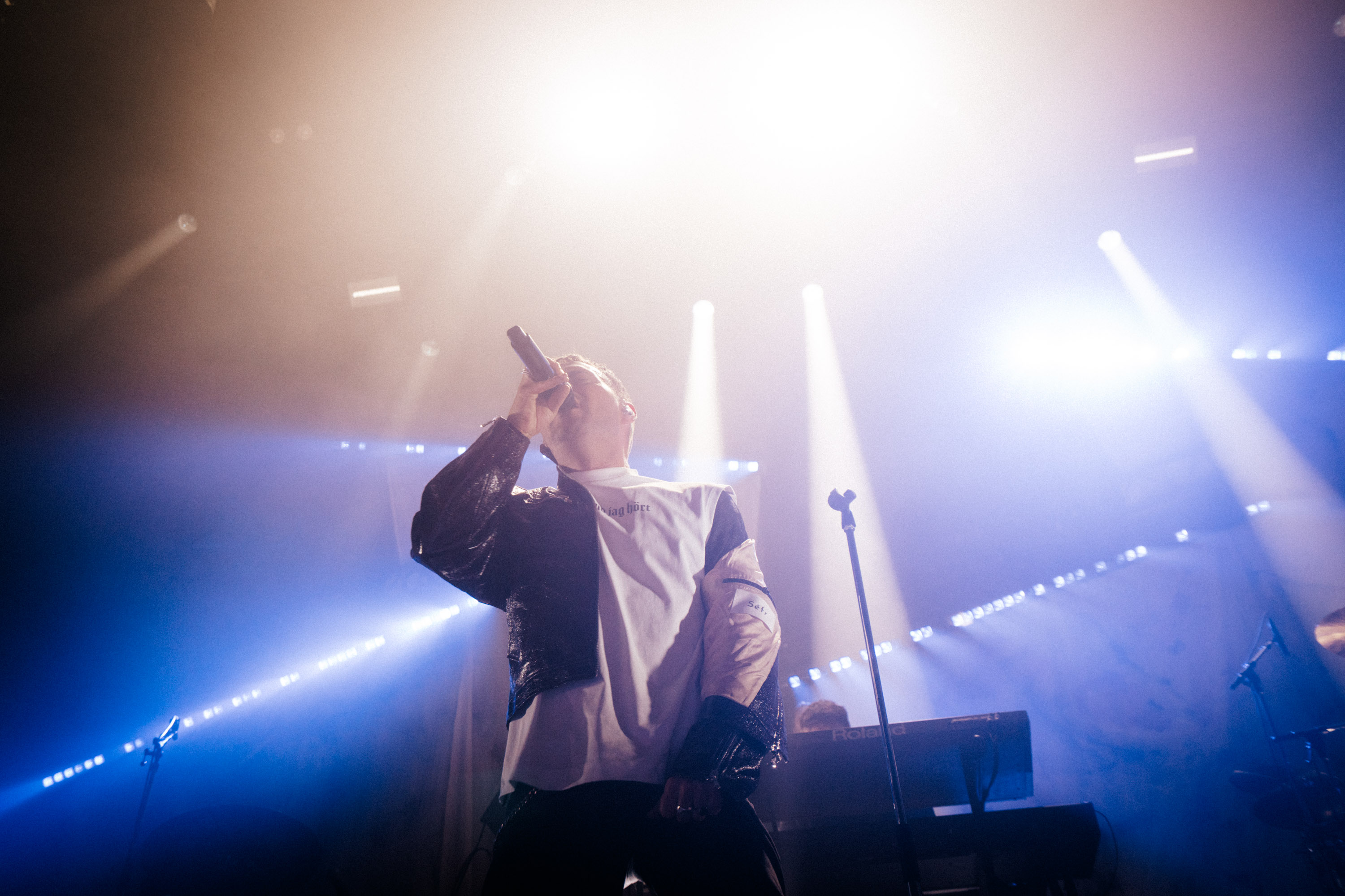 Oskar Linnros singing beneath blue and white concert lights